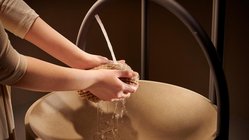 Eine Person hält einen Schwamm über ein rundes Waschbecken, während Wasser aus einem Wasserhahn fließt.