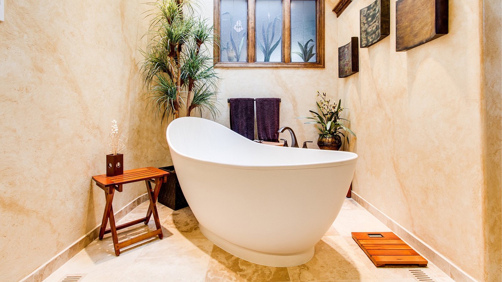 Ein elegantes Badezimmer mit einer freistehenden Badewanne, umgeben von Pflanzen und sanften Erdtönen an den Wänden.